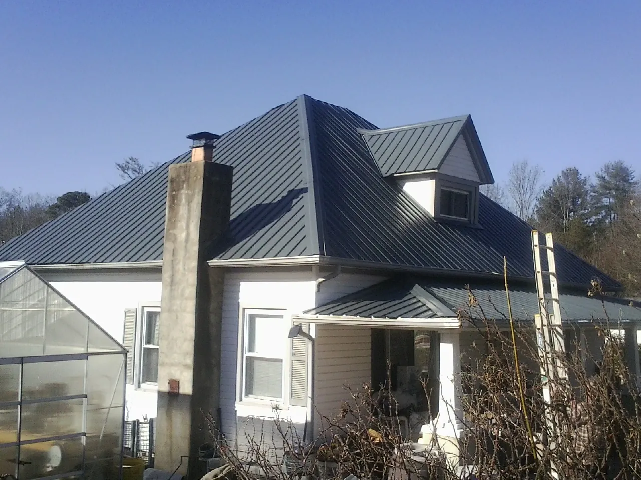 Dark blue standing seam metal roof on a white farmhouse with dormer — Slate & Tile Roof Repair by Roofing Brothers in North Canton