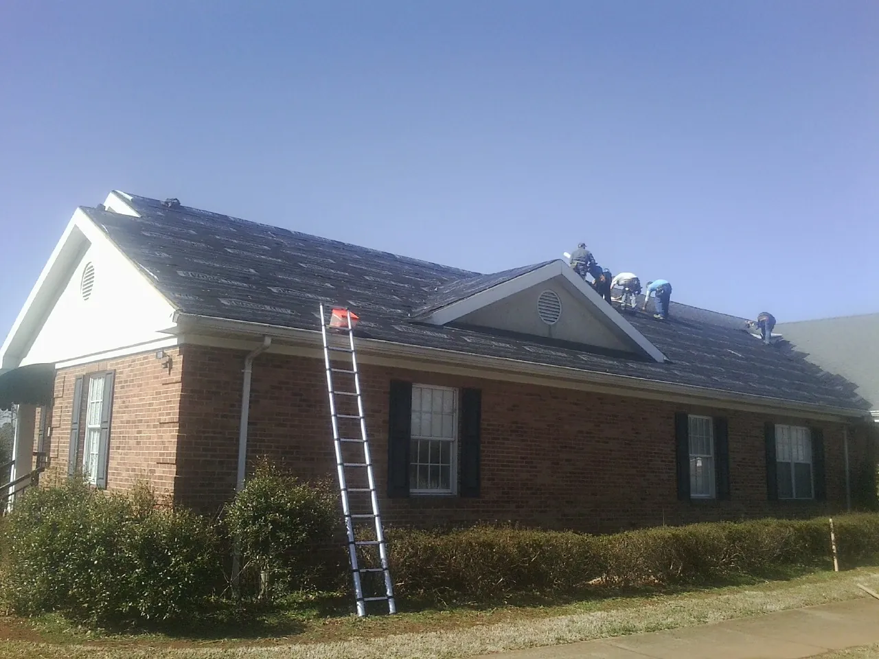 Crew tearing shingles off a brick ranch roof with a ladder set — Metal Roof Repair work by our crew in North Canton