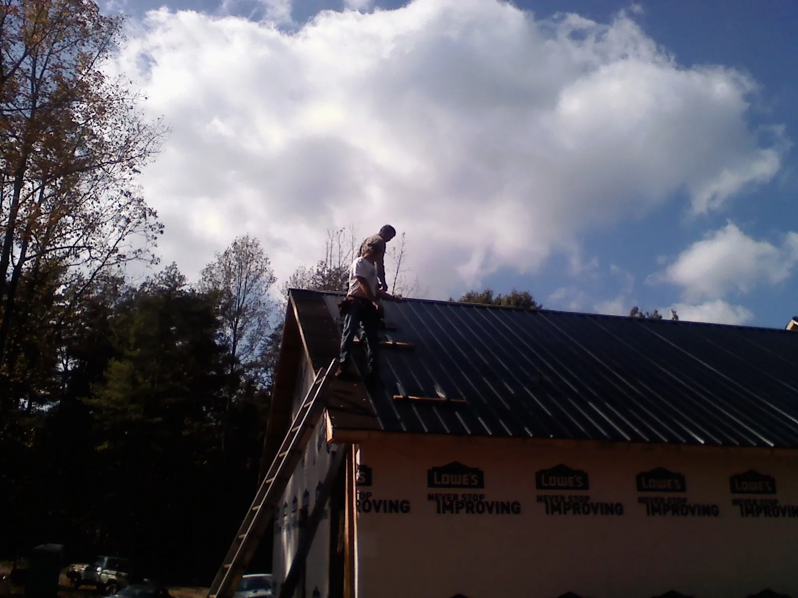 Roofer fastening dark metal panels high against a cloudy sky, from a Roof Inspection job in North Canton