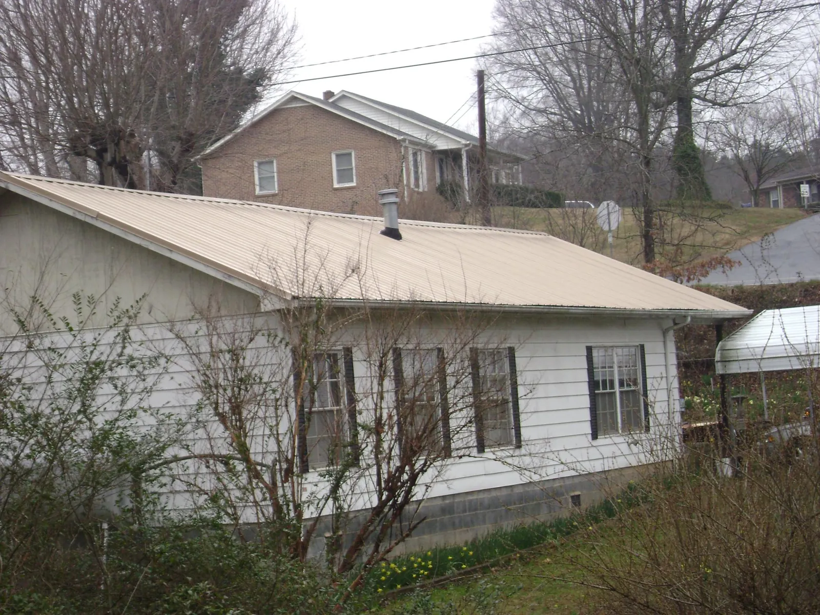 Tan metal roof on a white sided house set into a hillside — Commercial Roofing by Roofing Brothers in North Canton
